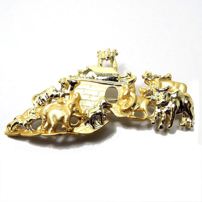 Front view of the retro vintage AJC Noah's Ark brooch pin. It is matte and shiny gold in color. The ark has an open doorway and is surrounded by a variety of animals.