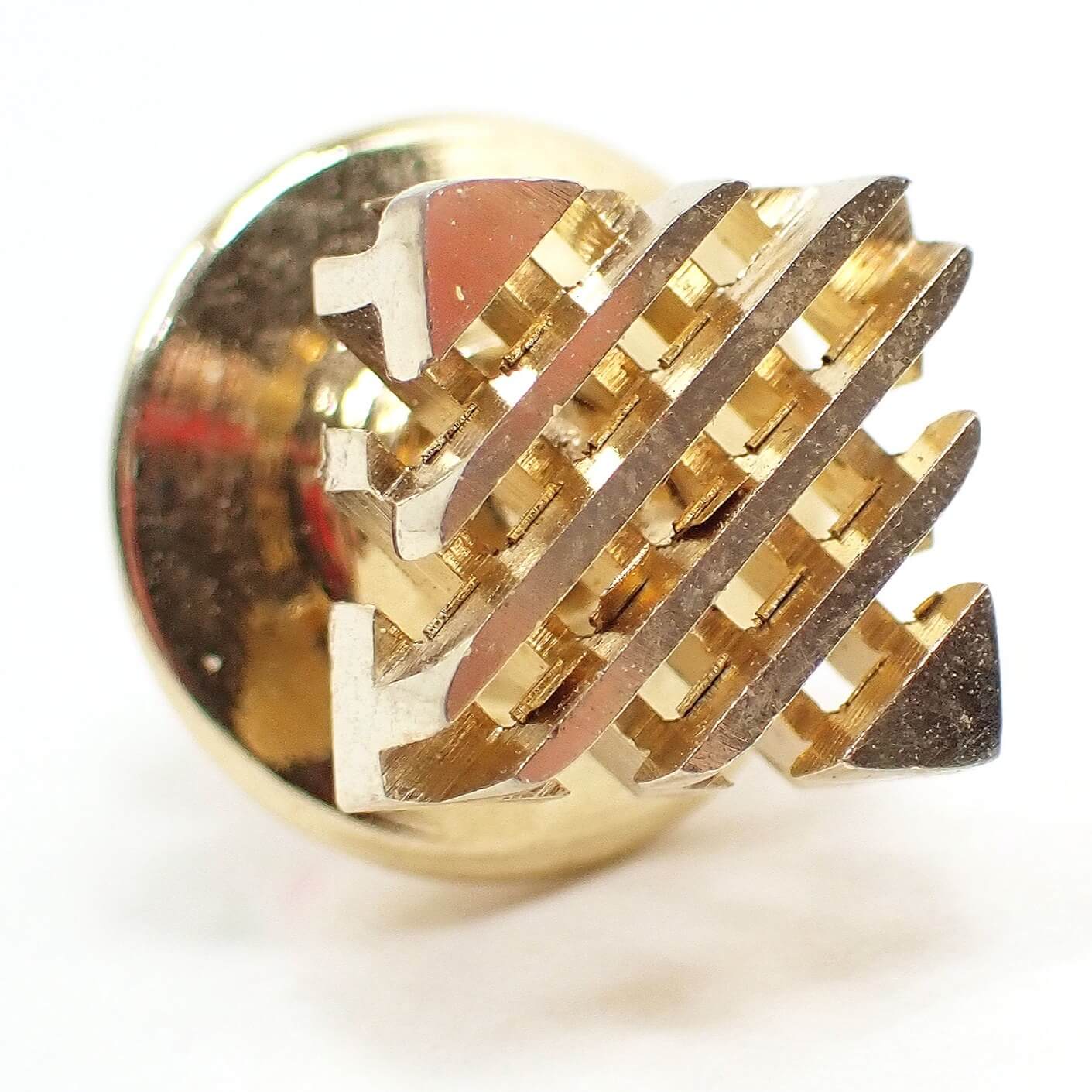 Enlarged angled view of the front of the retro vintage tie tack. It is gold tone in color. The tie tack is square with two layers of cut out diagonal lines. 