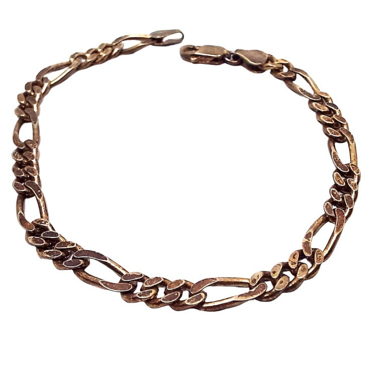 Top view of the retro vintage vermeil chain bracelet. It is a dark antiqued gold tone in color. The chain is figaro link which has three round links and then an oval link with faceted edges. There is a lobster claw clasp at the end.