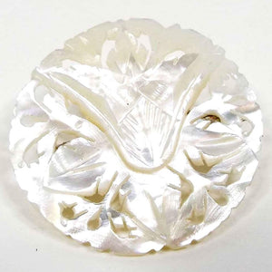 Front view of the Mid Century vintage brooch from Bethlehem. It is mostly round in shape and pearly white in color. The mother of pearl shell is carved with a floral and filigree design. 