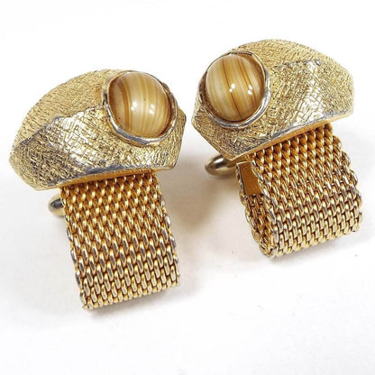 Front view of the Mid Century vintage mesh wrap around cufflinks. The metal is gold tone in color. The tops have a free form style shape with domed round fancy glass cabs. The glass has striped shades of brown, yellow, and cream colors.