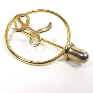 Front view of the retro vintage small initial stick pin. The metal is gold tone in color. There is an open wire circle with the letter L in fancy script inside it. The clutch goes onto the end just under the circle.