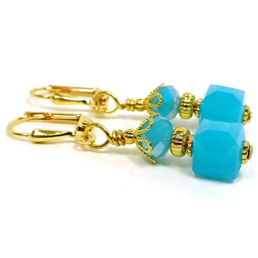 Side view of the small glass beaded earrings. The metal is gold plated in color. There are faceted glass crystal rondelle beads at the top and small cube shaped glass beads at the bottom. The beads are mint blue in color.