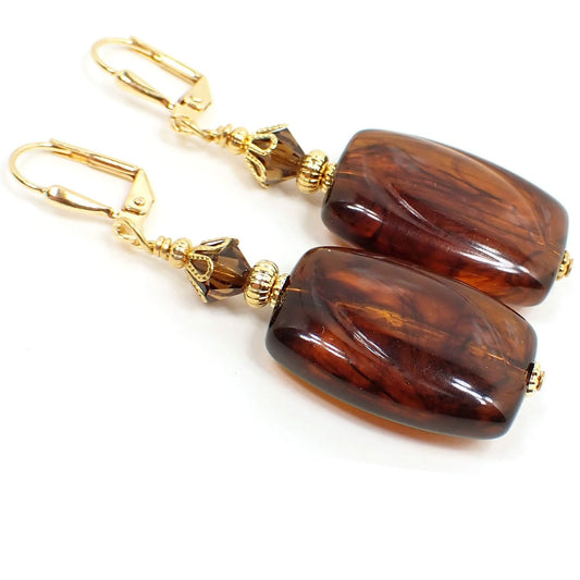 Side view of the handmade faux tortoise drop earrings. The metal is gold plated in color. There are faceted brown glass crystals at the top. The bottom beads are rectangle in shape with rounded edges and have an imitation tortoise design of marbled brown and black colors. 