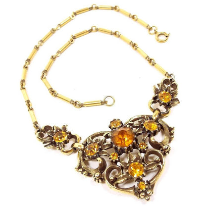 Front view of the Mid Century Vintage Coro rhinestone necklace. The metal is gold tone in color. There are three link areas at the bottom with citrine orange color rhinestones. There is a spring ring clasp at the end.