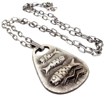 Front view of the retro vintage fish pendant necklace. The chain has flat oval cable links. There is a wide teardrop shaped flat pendant at the end with a raised design of three fish and a couple of waves. The fish and waves are primitive looking style and the pendant is pewter.