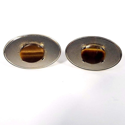 Front view of the Mid Century vintage Dante gemstone cufflinks. They are oval in shape and have matte gold tone color fronts. In the middle are oval tiger's eye gemstone cabs. 