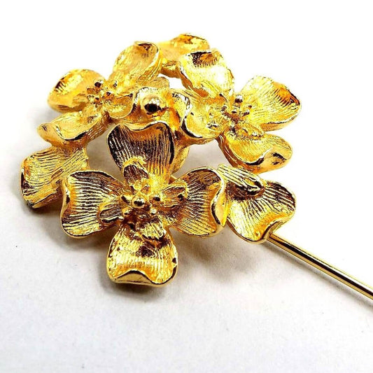 Enlarged top view of the Mid Century vintage Florenza floral stick pin. The metal is gold tone in color. There is a cluster of textured metal flowers at the top. 