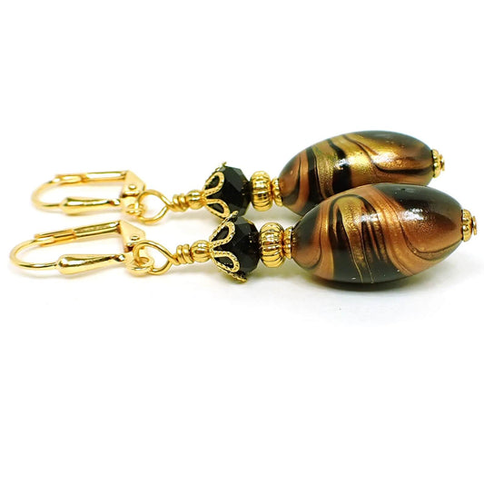 Side view of the handmade lucite earrings. The metal is gold plated in color. There are faceted black glass crystal beads at the top. The bottom lucite beads are black and oval in shape with marbled swirls of metallic gold and copper color. 
