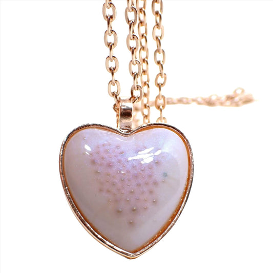 Front view of the handmade resin pink bubble heart pendant necklace. The metal is rose gold plated color. The front of the heart pendant has a domed resin cab with pearly color shift resin that is white with a sheen of blue as you move around. There are tiny pink bubbles in the middle of the heart.