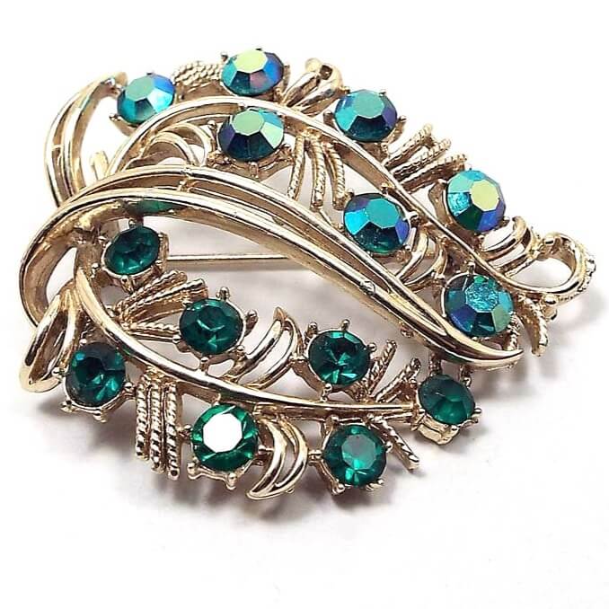 Front view of the Coro Mid Century vintage rhinestone brooch pin. The metal is gold tone in color. The brooch is shaped like a wide leaf and has AB green rhinestones on the top and green rhinestones on the bottom.