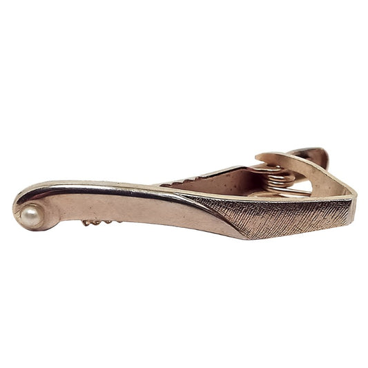 Front view of the Modernist style retro vintage tie clip. The metal is gold tone in color. It has a curved design with a plastic off white imitation pearl at the end.