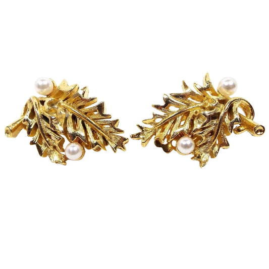 Front view of the Mid Century vintage Lisner clip on earrings. They are gold tone in color and shaped like a bunch of two leaves with white round imitation pearls on the sides.