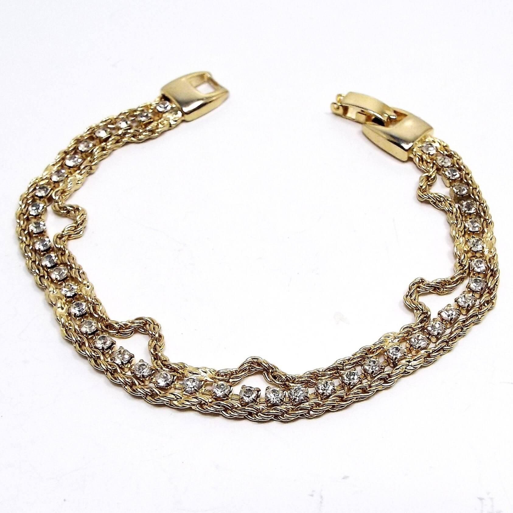 Top view of the retro vintage rhinestone bracelet. It is gold tone in color and has a strand of rhinestone cup chain in the middle with small round clear rhinestones. There is a strand of twisted rope chain on either side. 