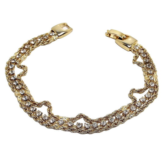 Top view of the retro vintage rhinestone bracelet. It is gold tone in color and has a strand of rhinestone cup chain in the middle with small round clear rhinestones. There is a strand of twisted rope chain on either side. 