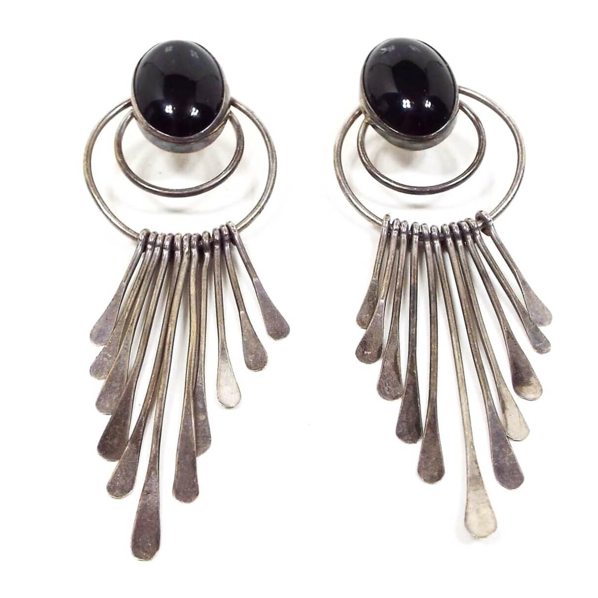 Front view of the retro vintage Nakai Chandelier Earrings. They are antiqued silver tone in color. There are ovals at the top with domed black onyx gemstone cabs. There are two wire rings underneath the onyx and the bottom ring has paddle shaped dangles of varying sizes making a fan like chandelier design.