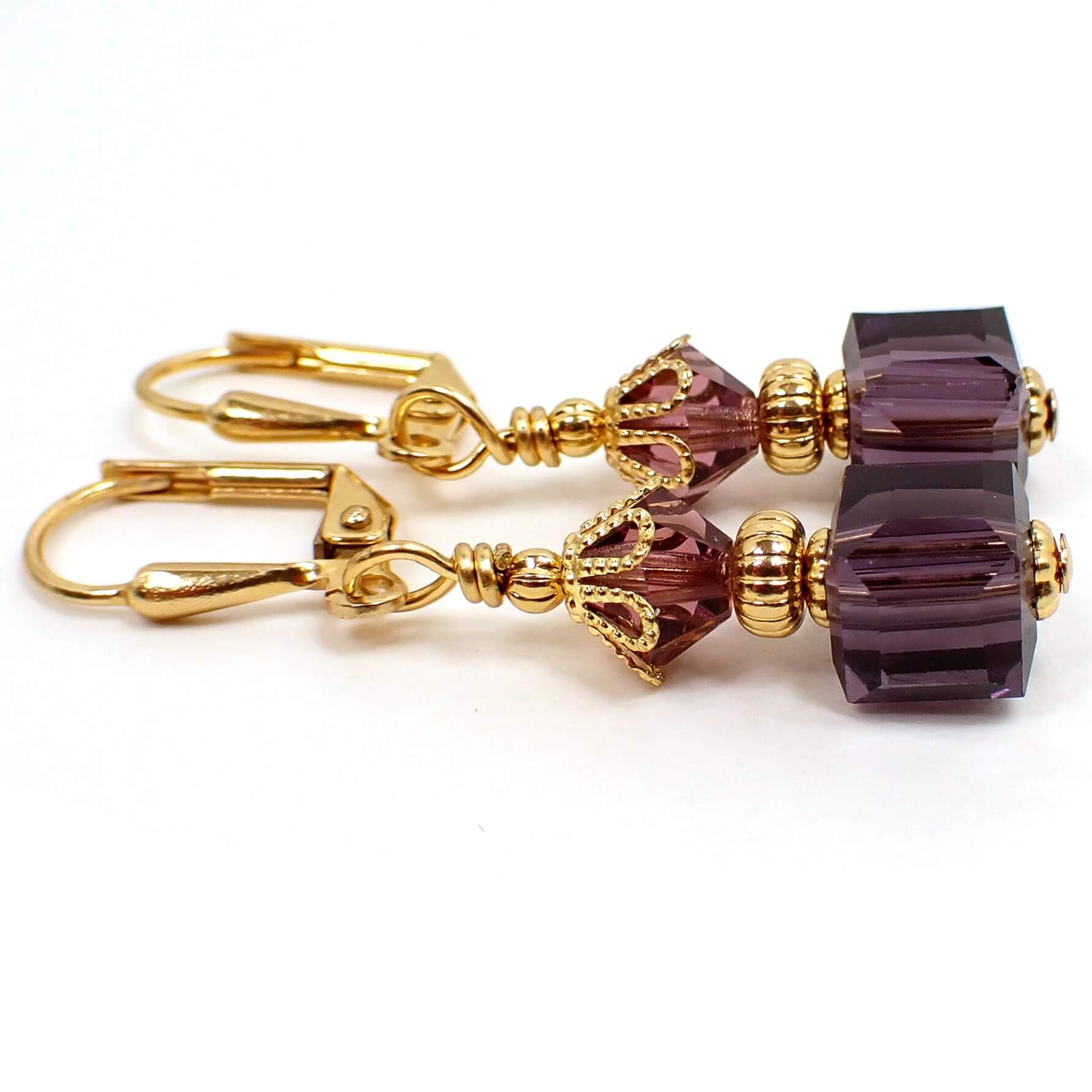 Side view of the small purple glass beaded earrings. The metal is gold plated in color. There are faceted glass crystal bicone beads at the top and small cube shaped glass beads at the bottom. The beads are purple in color.