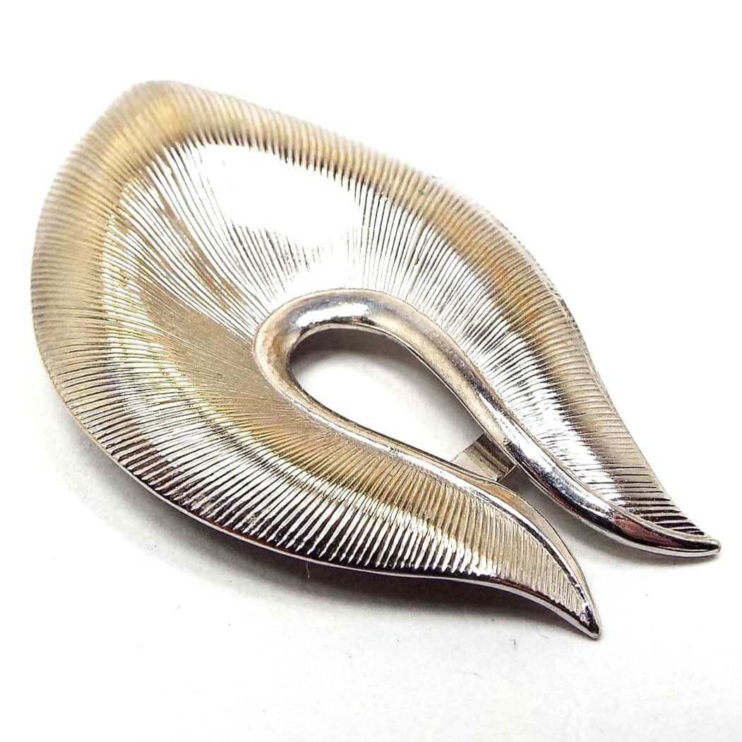 Front view of the retro vintage textured silver tone scarf clip. It has an angled sort of teardrop shape with a teardrop dip in the top area. There is a textured line pattern all the way around the clip.