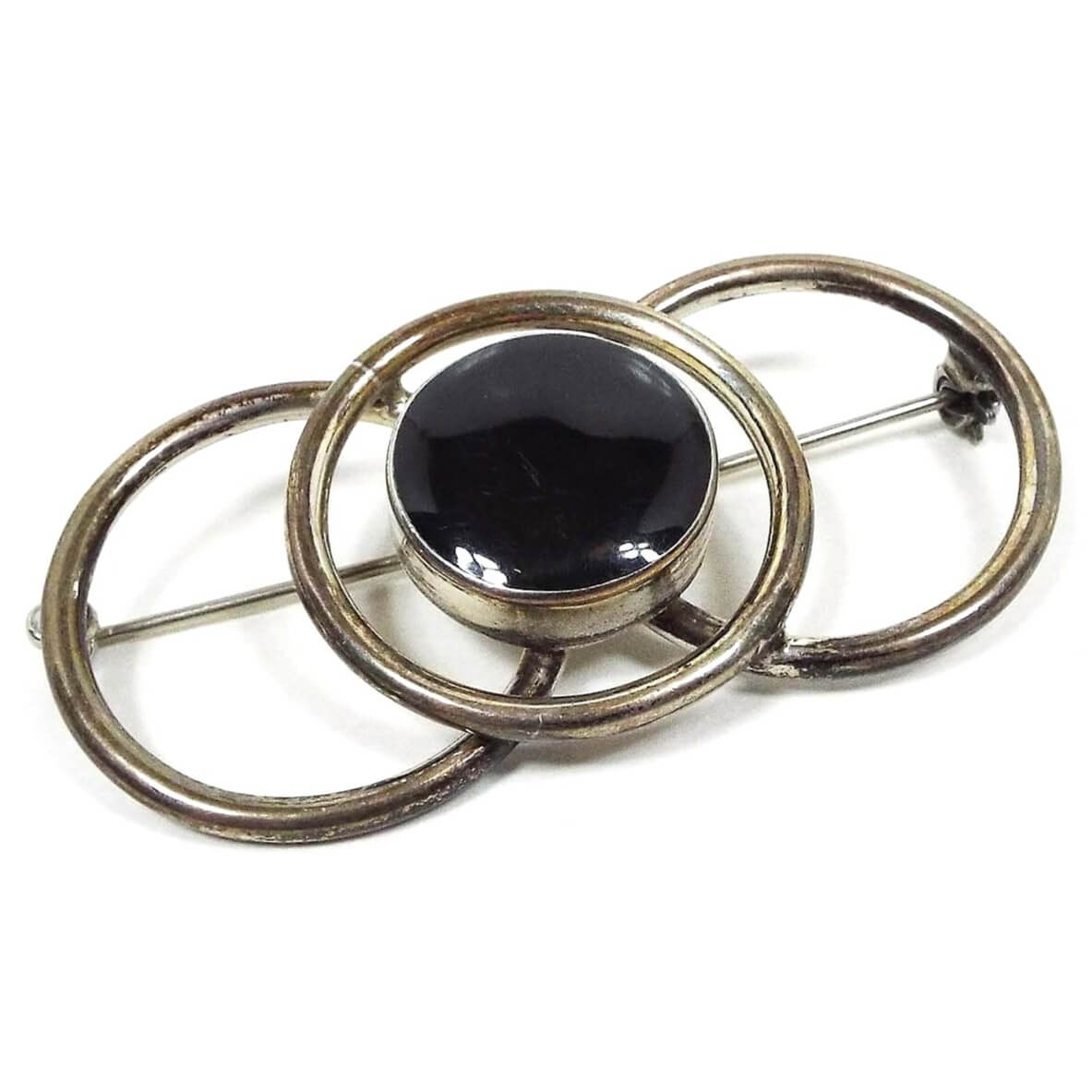 Front view of the retro vintage Taxco brooch pin. The sterling silver is darkened from age to a dark gray and even black in some areas. There are three open circles that overlap making up the brooch. The middle circle has a round area in the middle of it with black enamel. 