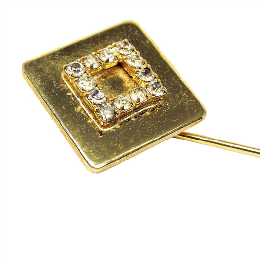 Enlarged view of the top part of the retro vintage rhinestone stick pin. The metal is gold tone in color. There is a larger diamond shape at the top with prong set round clear rhinestones in the middle area.