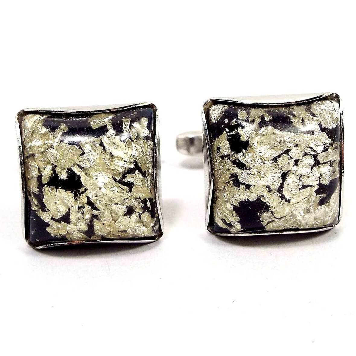 Front view of the Hickok Mid Century vintage confetti lucite cufflinks. They are square with silver tone color metal. The front cabs are black with pieces of metallic silver foil, and is topped with clear lucite that has slightly yellowed from age giving some of the foil pieces a light gold color depending on angle and lighting.