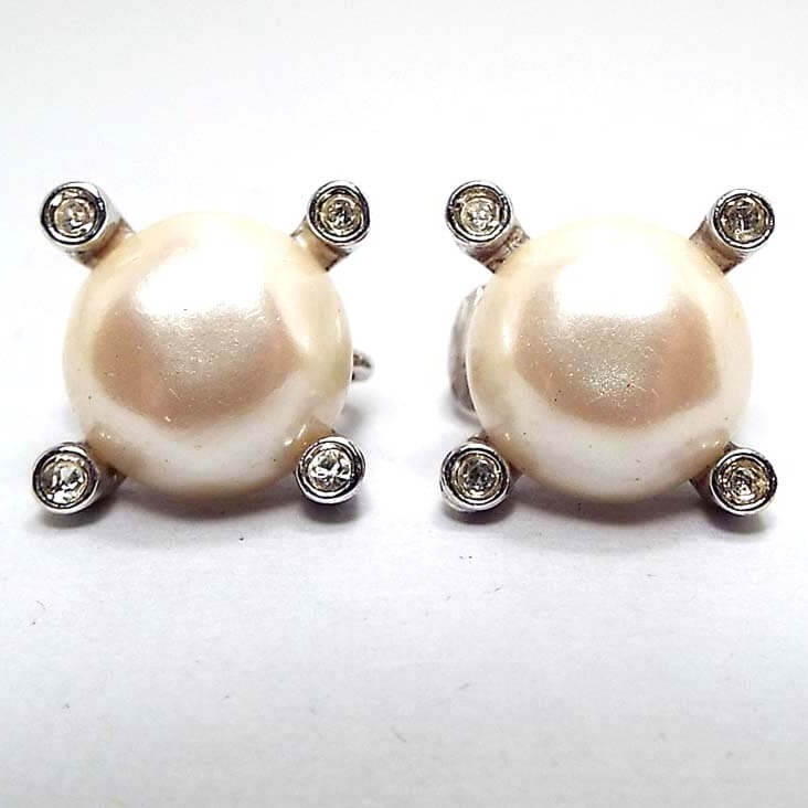 Front view of the retro vintage Avon rhinestone and faux pearl clip on earrings. The imitation pearls are round plastic cabs in an off white color in the middle. There is a round clear rhinestone at each corner of the earrings.