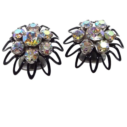 Angled front view of the Mid Century vintage Japanned AB rhinestone clip on earrings. The are shaped like flowers with open wire style petals. The setting is black enameled. There are aurora borealis rhinestones set in the middle of the flowers with six smaller sized AB rhinestones around them.