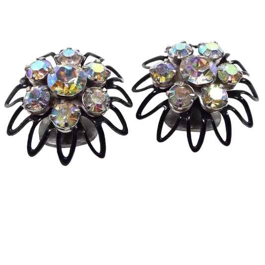 Angled front view of the Mid Century vintage Japanned AB rhinestone clip on earrings. The are shaped like flowers with open wire style petals. The setting is black enameled. There are aurora borealis rhinestones set in the middle of the flowers with six smaller sized AB rhinestones around them.