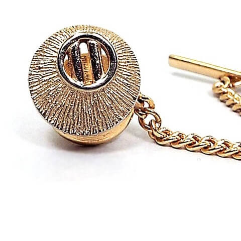 Enlarged front view of the Mid Century vintage Swank tie tack. It is round in shape and gold tone in color with a matte textured front. There is a round cut out area at the top with two bars in it .
