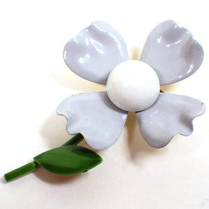 Front view of the Mid Century vintage enameled floral brooch pin. It is shaped like a large flower with four gray petals and a light gray center. The stem and leave are green. There is some wear showing on the enamel around the very edges of the flower petals.