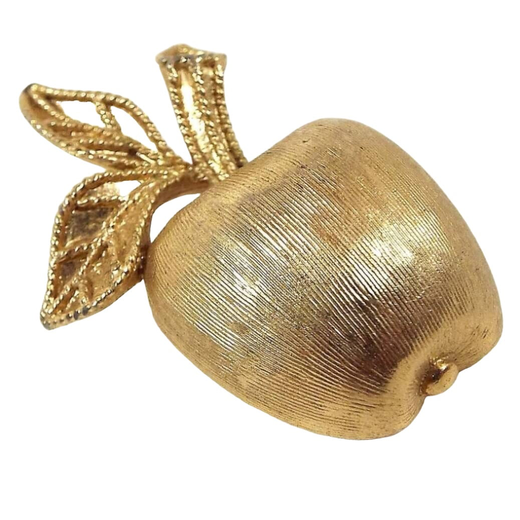 Front view of the retro vintage Avon apple brooch pin. It is gold tone in color and has a textured surface. It's shaped like an apple with stem and two leaves.