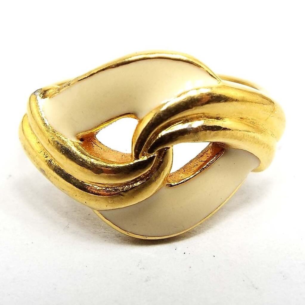 Front view of the retro vintage enameled ring. The metal is gold tone in color. The top has a twist design with curves of cream color enameled metal in the back with curves of gold tone metal over the front.