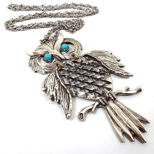 Front view of the retro vintage articulated owl pendant necklace. The metal is silver tone in color. The necklace has a twisted rope chain and the large owl pendant has three parts linked with round jumprings. The owl has two blue plastic eyes. 