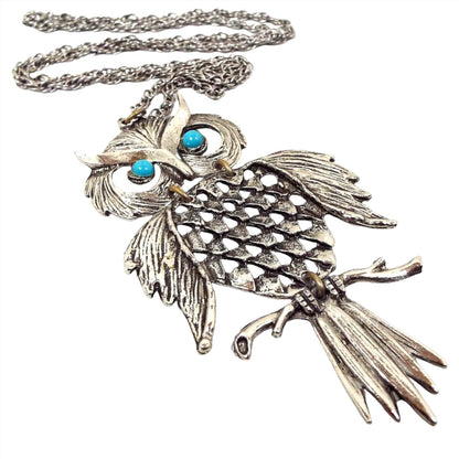 Front view of the retro vintage articulated owl pendant necklace. The metal is silver tone in color. The necklace has a twisted rope chain and the large owl pendant has three parts linked with round jumprings. The owl has two blue plastic eyes. 