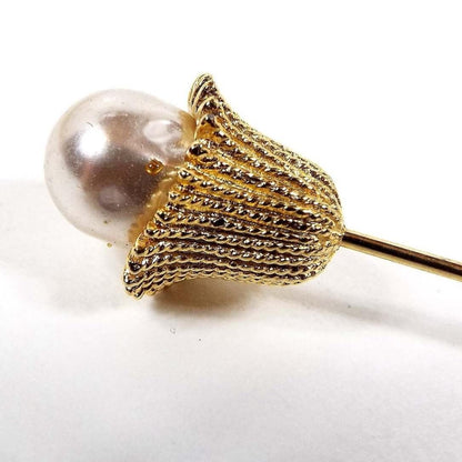 Enlarged top view of the Mid Century vintage faux pearl stick pin. The metal is gold tone and has an upside down bell shape on the top with a teardrop shaped imitation pearl coming out of it. 