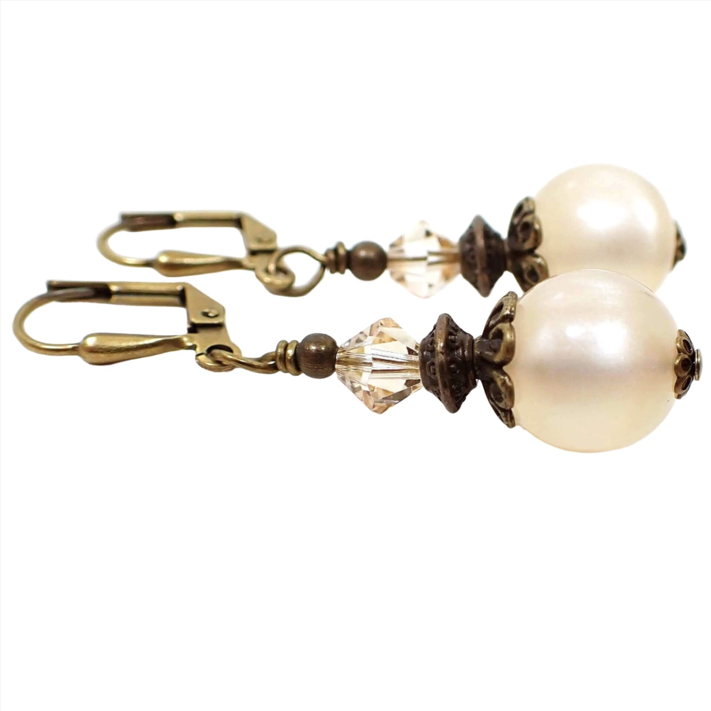 Side view of the handmade drop earrings with vintage lucite beads. The metal is antiqued brass in color. There are faceted glass bicone beads at the top in a very light champagne color. The bottom beads are round moonglow lucite in an off white color. They have a glowy effect as you move around in the light.