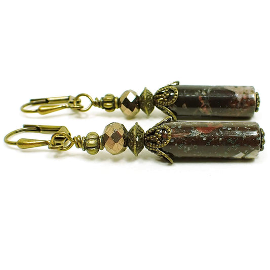 Side view of the handmade portoro marble earrings. The metal is antiqued brass in color. There are faceted metallic bronze color glass beads at the top and tube shaped gemstone beads at the bottom. The marble beads have shades of brown and cream color.