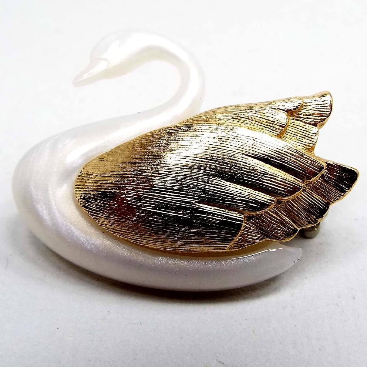 Front view of the retro vintage Avon swan brooch pin. It is pearly white in color and has gold tone color textured metal wings.