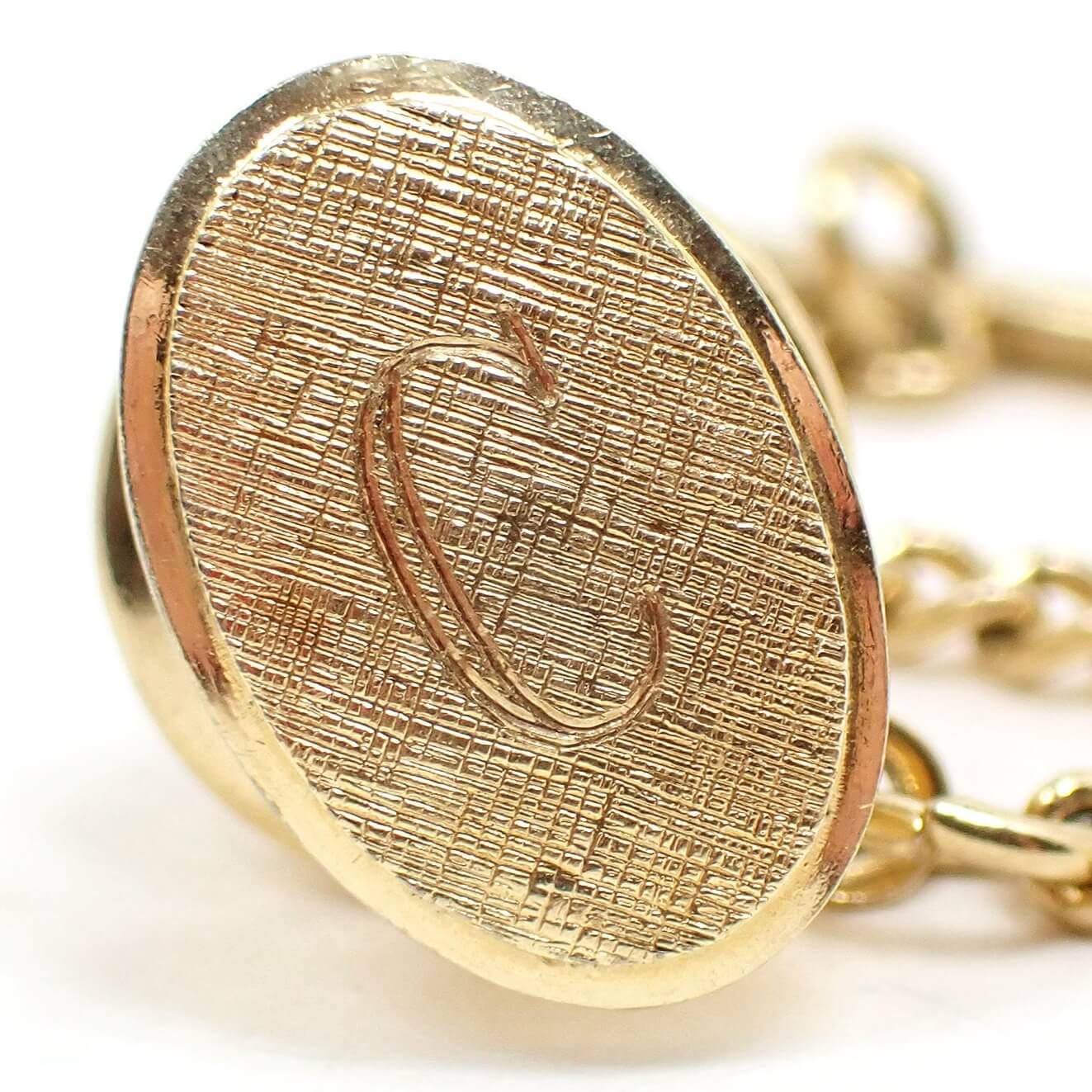 Enlarged front view of the Mid Century vintage initial tie tack. It is oval and has a brushed matte gold tone appearance. There is a block style letter C engraved on the front.