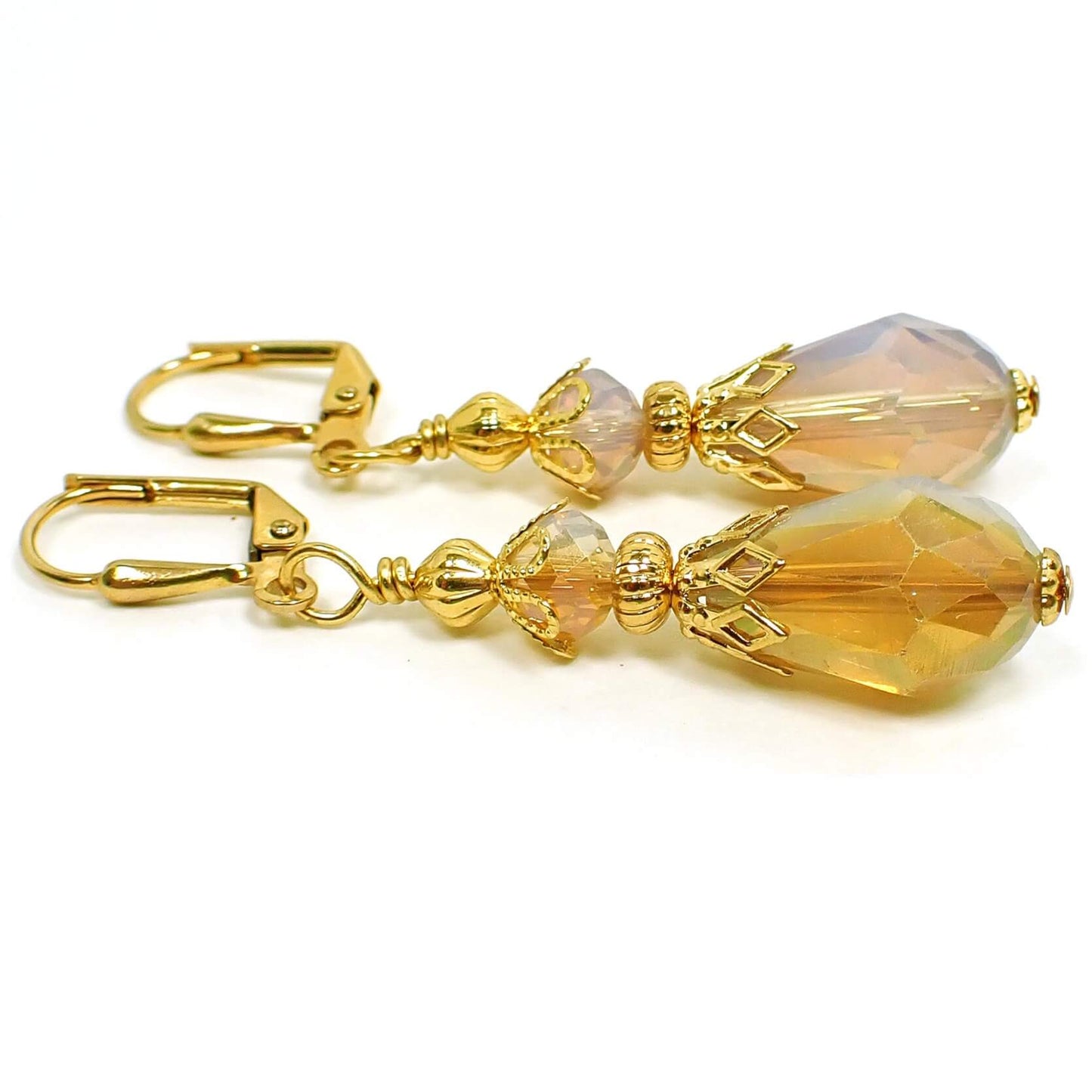 Side view of the handmade half and half teardrop earrings. The metal is gold plated in color. The faceted glass crystal beads are half dark peach color and half opal glass color. The bottom beads are teardrop shaped.