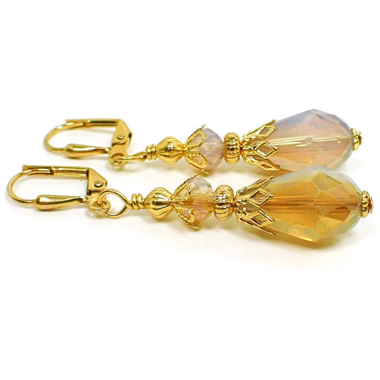 Side view of the handmade half and half teardrop earrings. The metal is gold plated in color. The faceted glass crystal beads are half dark peach color and half opal glass color. The bottom beads are teardrop shaped.