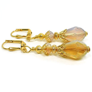 Side view of the handmade half and half teardrop earrings. The metal is gold plated in color. The faceted glass crystal beads are half dark peach color and half opal glass color. The bottom beads are teardrop shaped.