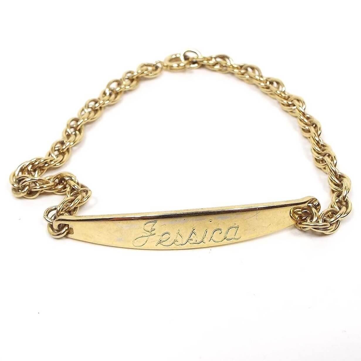 Angled front view of the retro vintage ID bracelet. It is gold tone in color with a twisted rope chain style chain. The front angled panel has the name Jessica engraved on it. There is a spring ring clasp on the end.