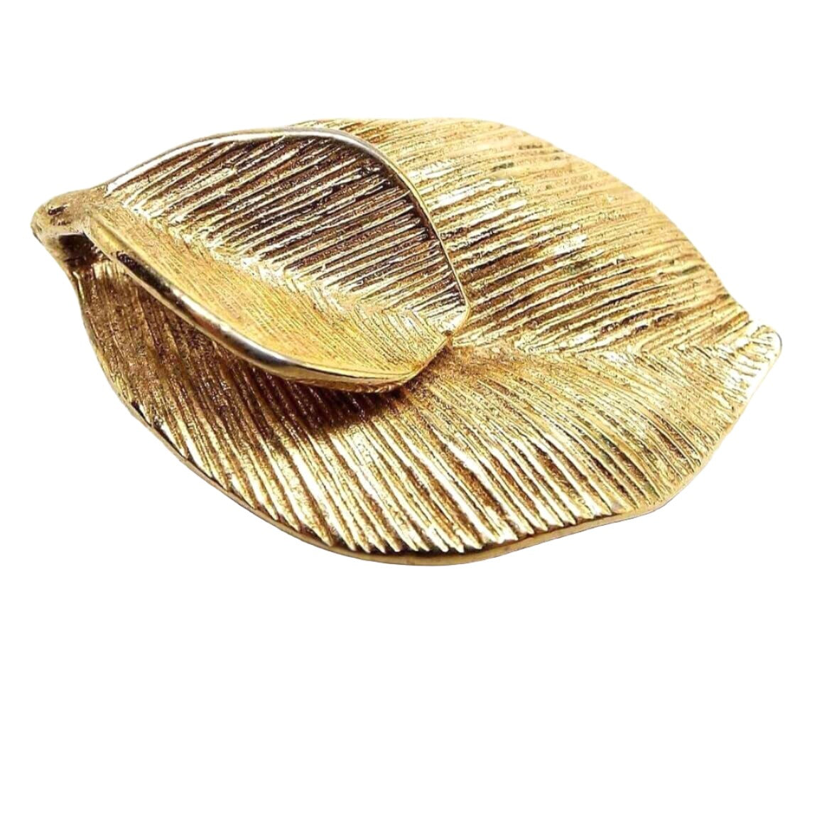 Top view of the Amway retro vintage leaf brooch pendant. It is gold tone in color. It has a double leaf design with the larger one on the bottom. There is a curved space at the top by the stem for a chain to go through.  The leaves are textured.
