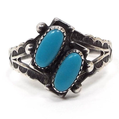 Front view of the retro vintage Southwestern sterling turquoise ring. The silver has been aged so the recesses have a dark gray appearance. There are two diagonal oval blue turquoise cabs on the top that are bezel set on top of rectangle sterling. There are two dots of sterling on each side . The band is split at the top and has a half moon with stripes stamped design down to the sides. 