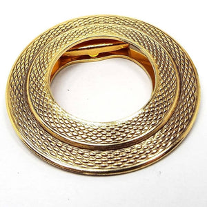 Front view of the retro vintage Lieba scarf clip. It has a double round design with a textured diamond shape scale like pattern. The metal is gold tone in color.