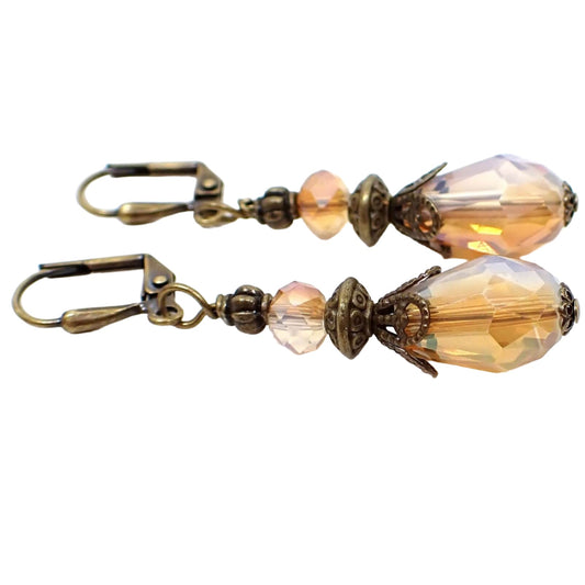 Side view of the handmade half and half teardrop earrings. The metal is antiqued brass in color. The faceted glass crystal beads are half peach color and half opal glass color. The bottom beads are teardrop shaped.