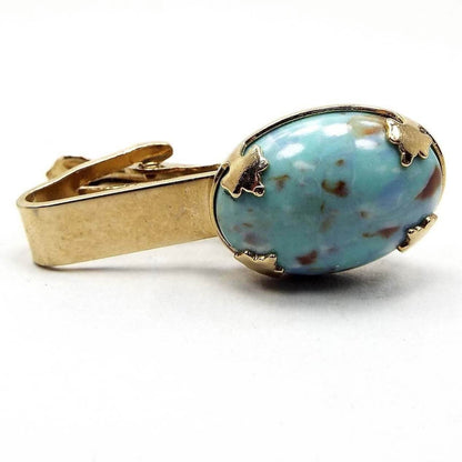 Front view of the Mid Century vintage blue lucite tie clip. The metal is gold tone in color. At the end is a large oval lucite cab in light blue with brown and white speckles like a robin's egg. 