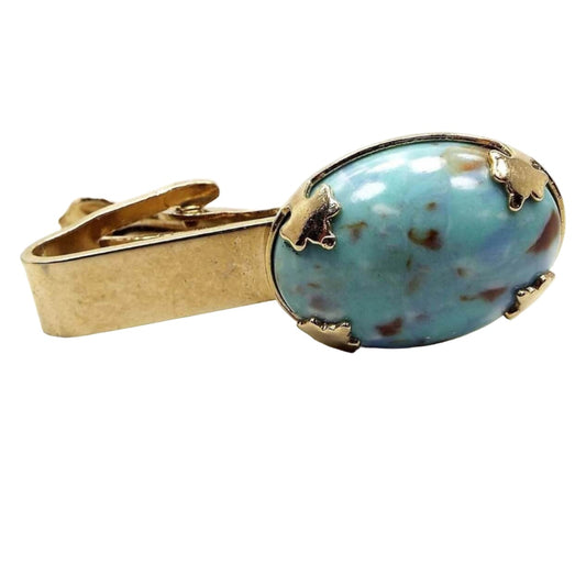 Front view of the Mid Century vintage blue lucite tie clip. The metal is gold tone in color. At the end is a large oval lucite cab in light blue with brown and white speckles like a robin's egg. 