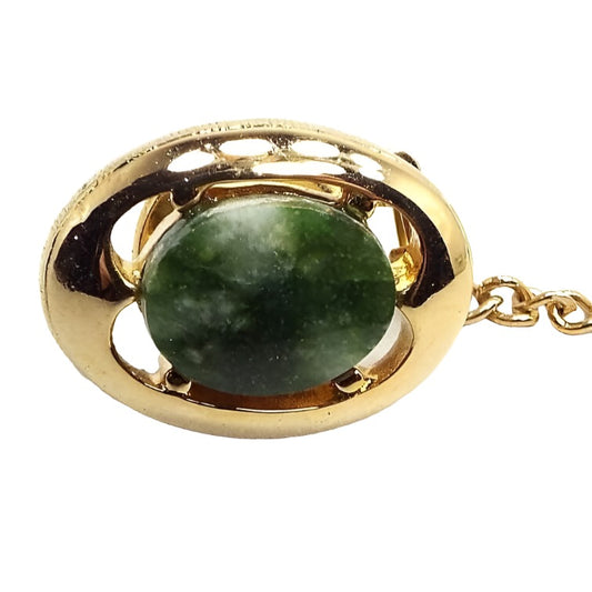 Enlarged view of the Mid Century vintage moss agate tie tack. The tie tack is oval in shape and gold tone in color. There is an oval mossy green gemstone cab in the middle.